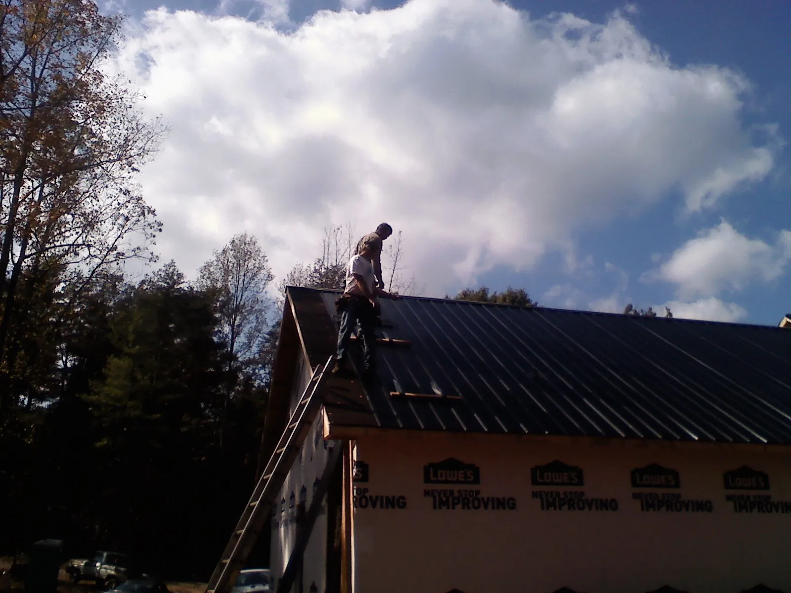 Roofer fastening dark metal panels high against a cloudy sky, from a Roof Inspection job in Diamond Bar