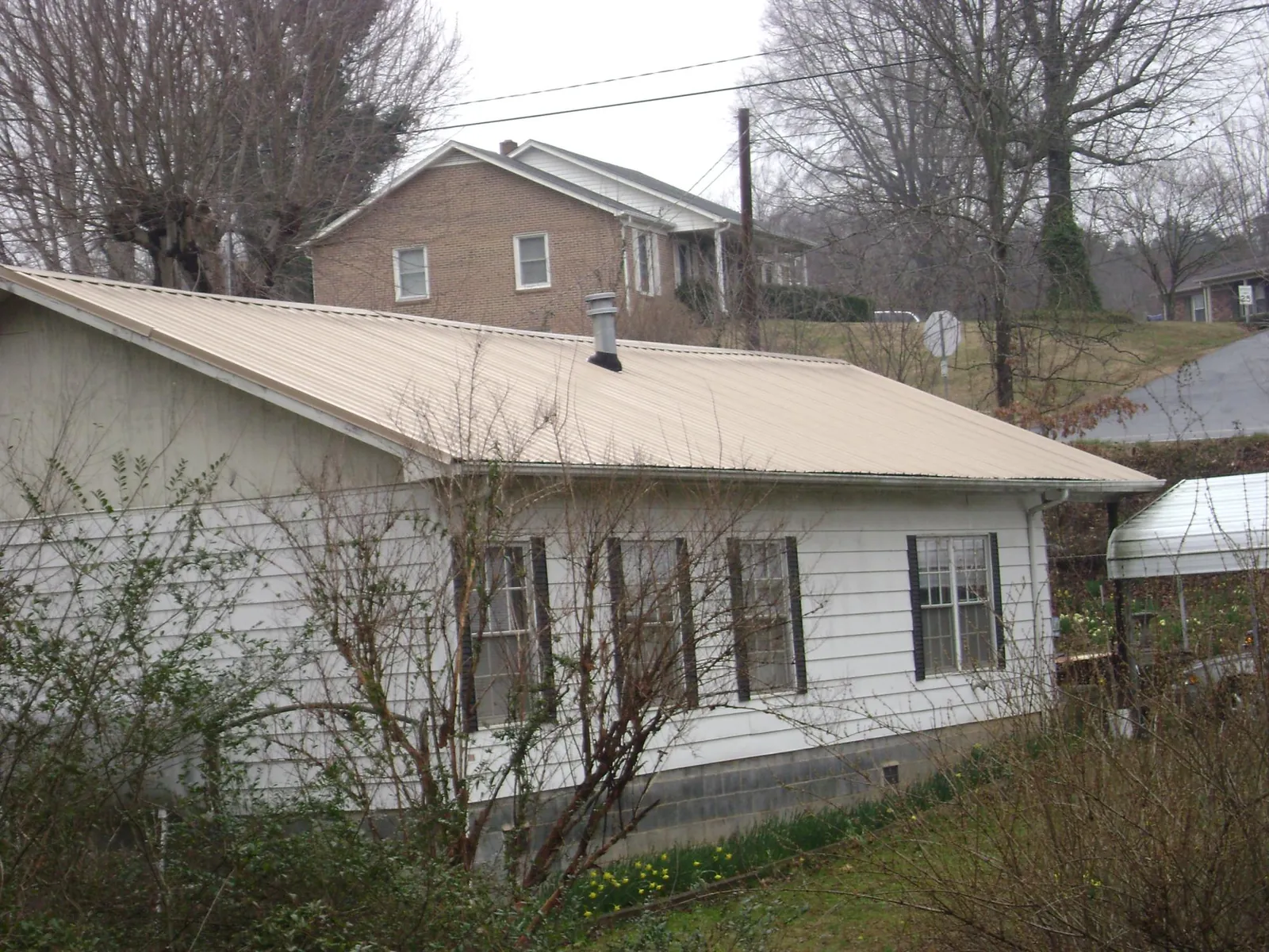 Tan metal roof on a white sided house set into a hillside — Commercial Roofing by Roofing Brothers in Diamond Bar